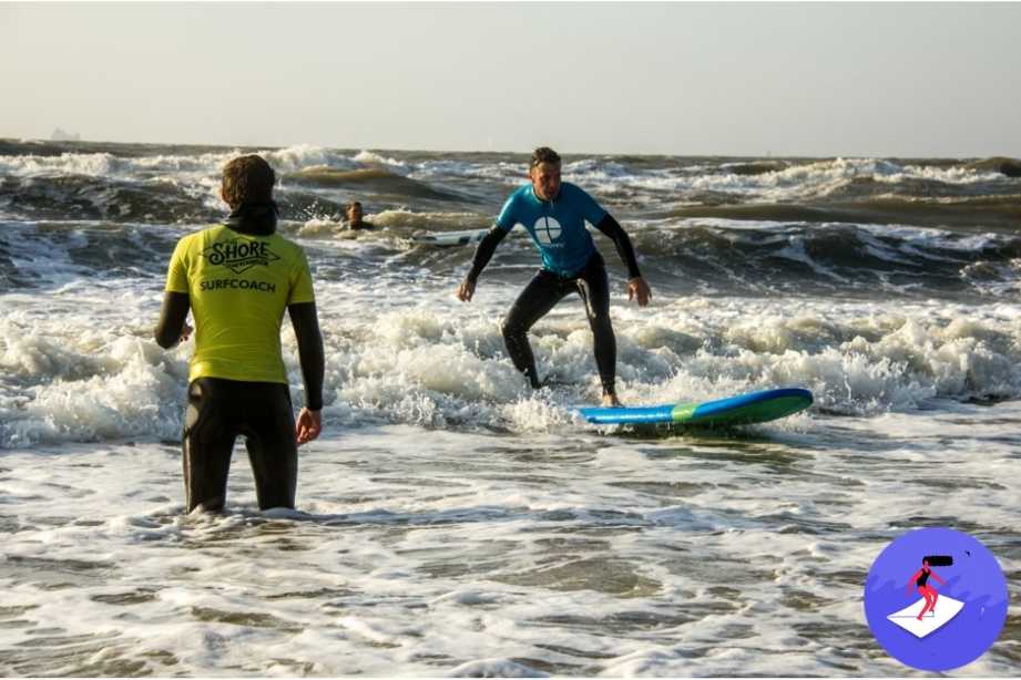 Jongen staat op surfplank met instructeur in de zee